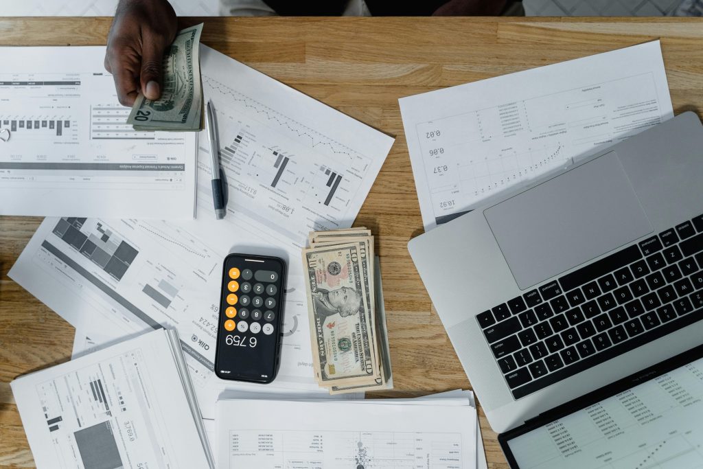 Overhead view of a busy workspace with cash, financial documents, and a laptop.