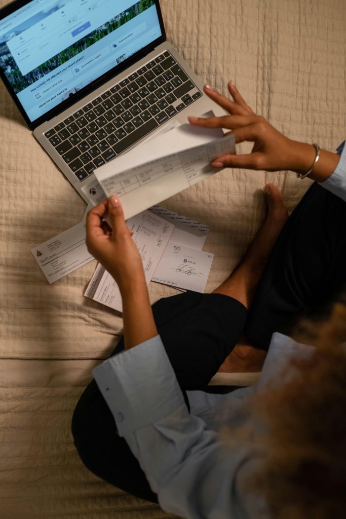 Woman holding checks while managing finances on a laptop, showing online banking on the screen.